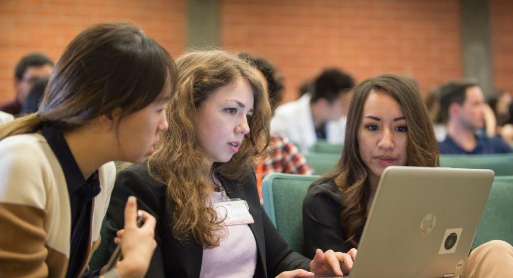 Photos shows three PA students at UOP gathered around a laptop in a lecture hall. 