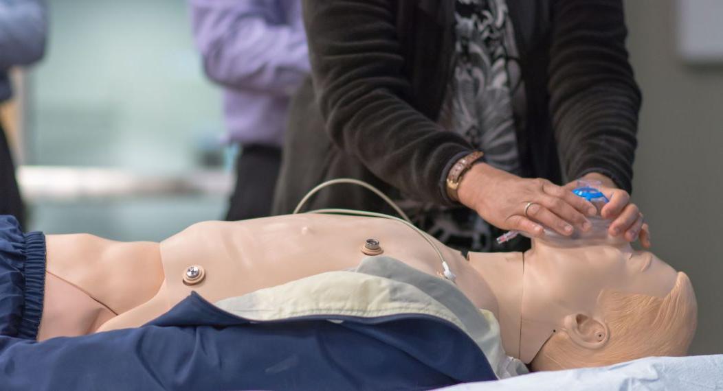 Photo shows a student standing next to a manikin while practicing putting on a breathing mask. 